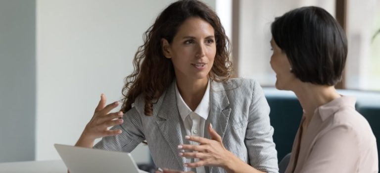 Due donne che parlano in ufficio durante una sessione di business coaching, simbolo di collaborazione, chiarezza strategica e crescita professionale guidata da un coach esperto