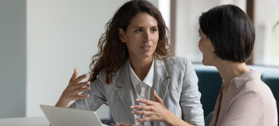 Due donne che parlano in ufficio durante una sessione di business coaching, simbolo di collaborazione, chiarezza strategica e crescita professionale guidata da un coach esperto