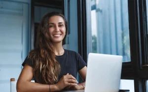 Donna sorridente in ufficio che esprime fiducia in se stessa, simbolo di crescita personale e autostima potenziata grazie al coaching professionale