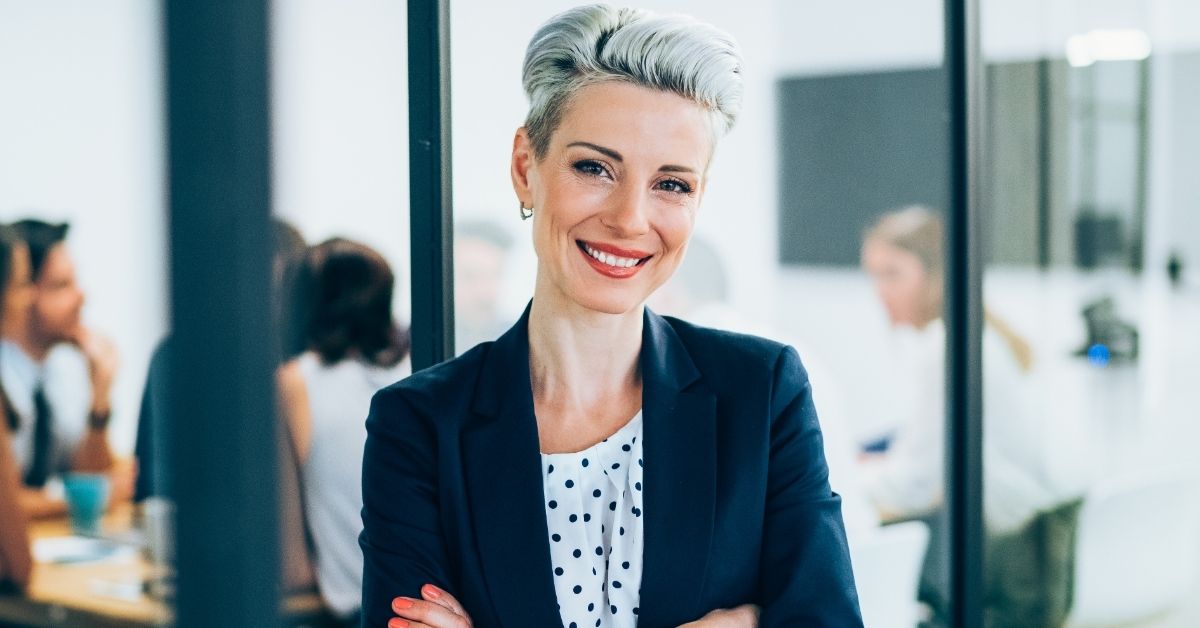 Donna sorridente e soddisfatta in ufficio, simbolo di successo professionale e crescita nel costruire una clientela di coaching solida ed efficace