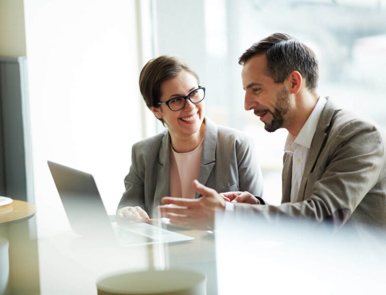 Donna e uomo seduti in ufficio davanti a un laptop che discutono di lavoro, simbolo di collaborazione, performance e produttività migliorate grazie al business coaching.