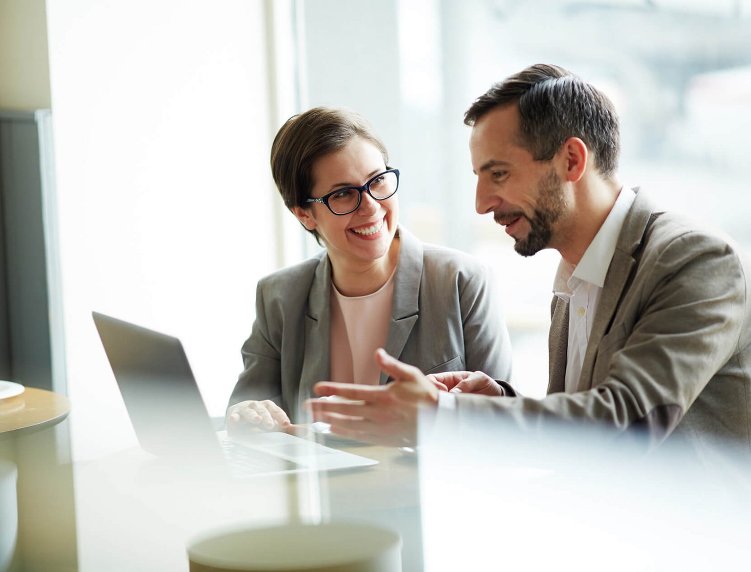Donna e uomo seduti in ufficio davanti a un laptop che discutono di lavoro, simbolo di collaborazione, performance e produttività migliorate grazie al business coaching.