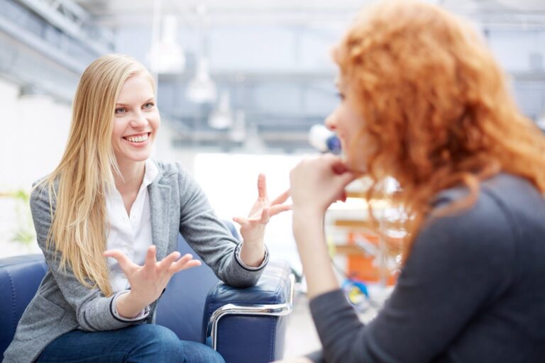 Due donne in ufficio che parlano con entusiasmo durante una sessione di coaching, simbolo di fiducia, confronto costruttivo e crescita professionale per coach e clienti